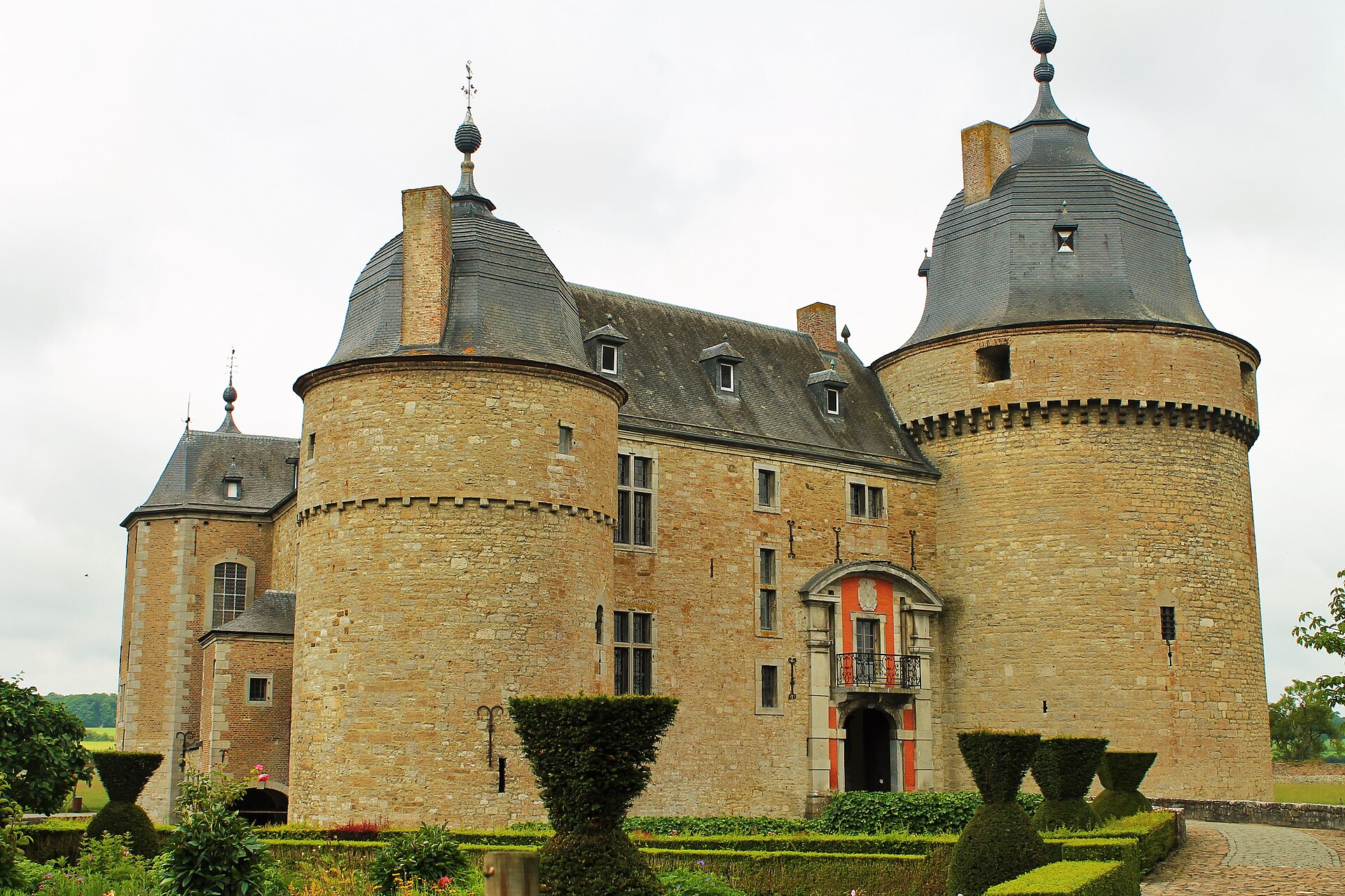 The twin bell-roofed round towers and ornate entrance of Château de Lavaux-Sainte-Anne above its topiary garden