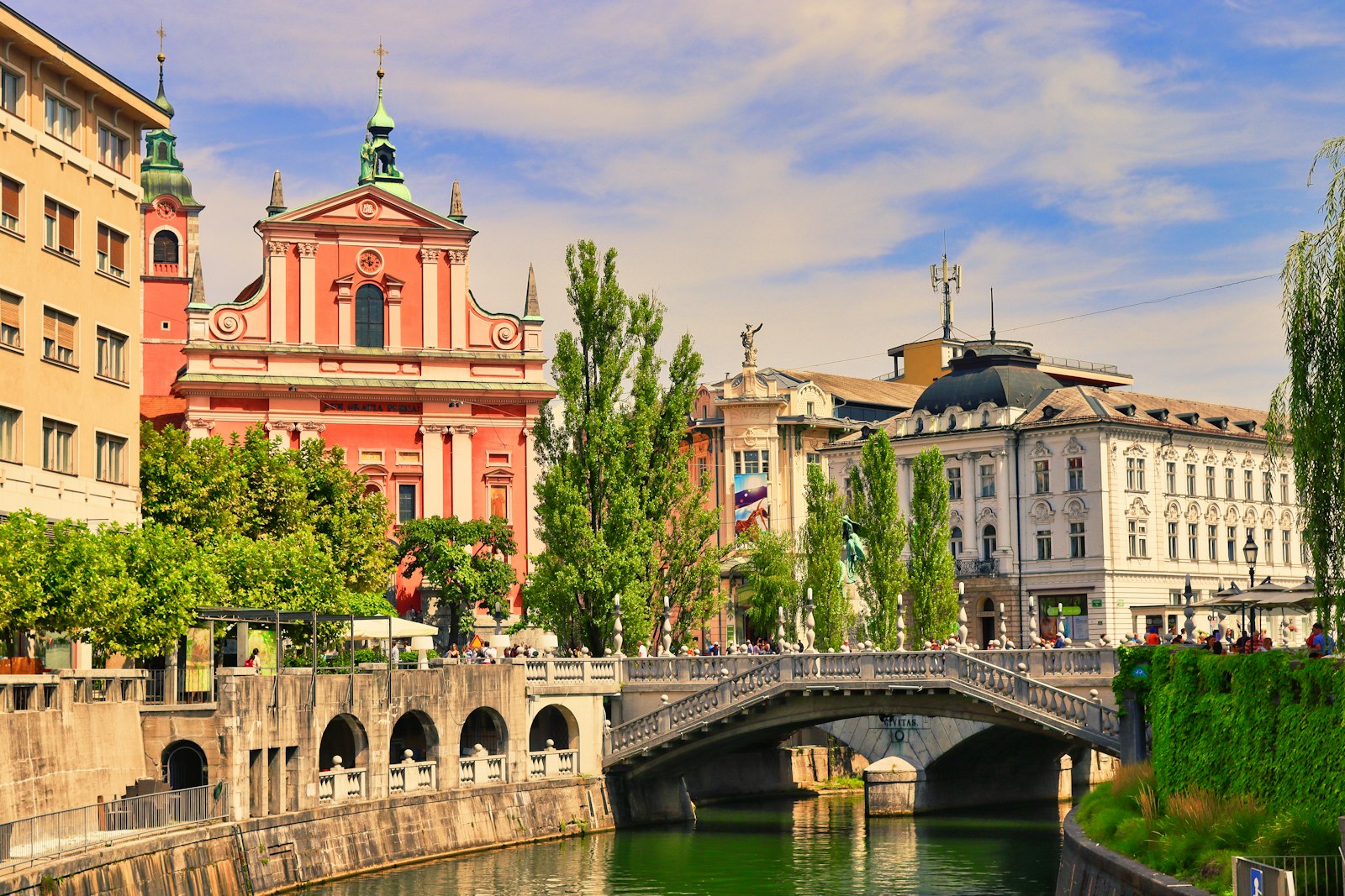Ljubljana's riverside cafés and pastel façades below a hilltop castle, with a dragon-topped bridge