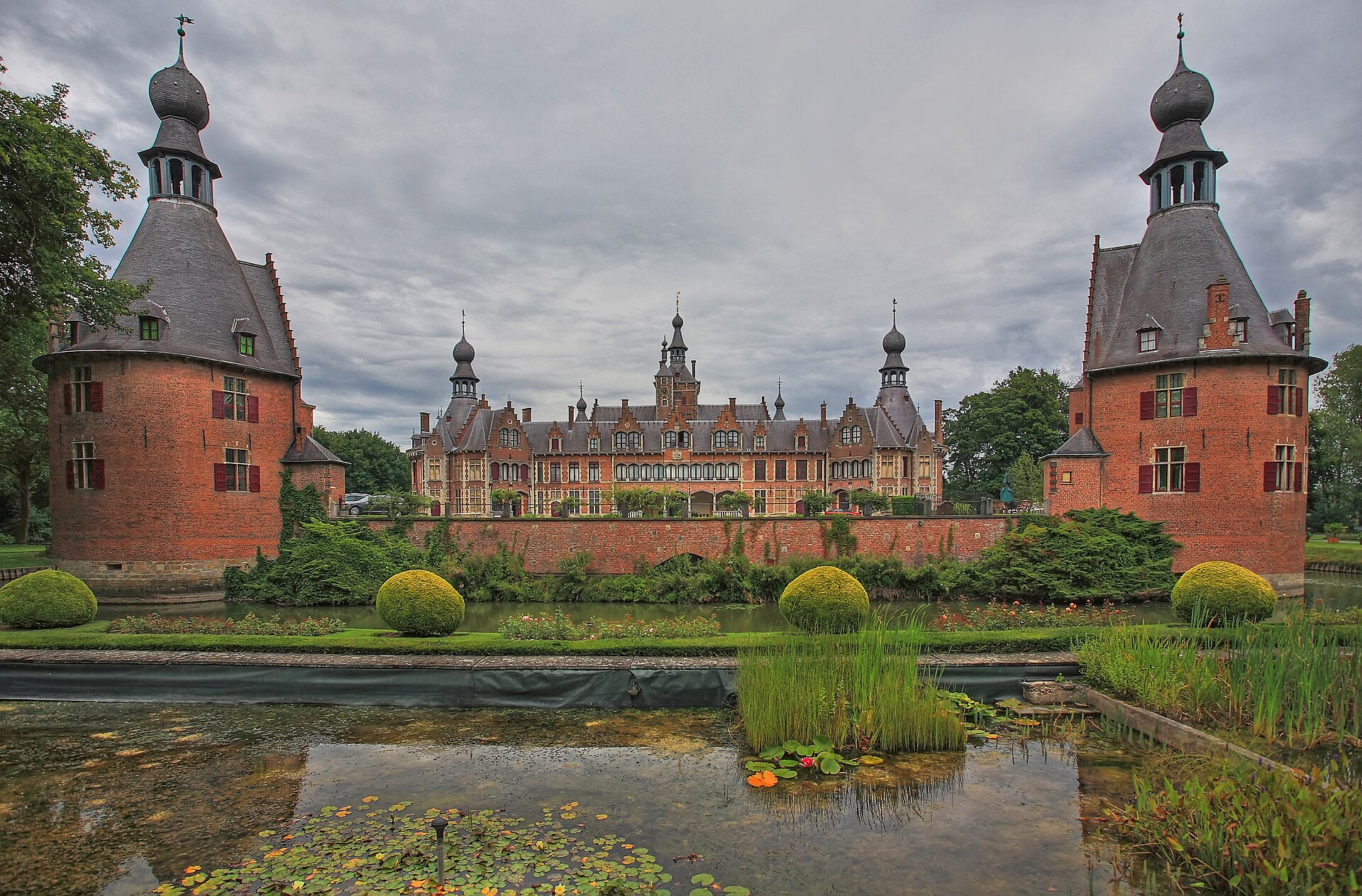 The onion-domed brick towers of Kasteel van Ooidonk framing its château and garden pond near Deinze