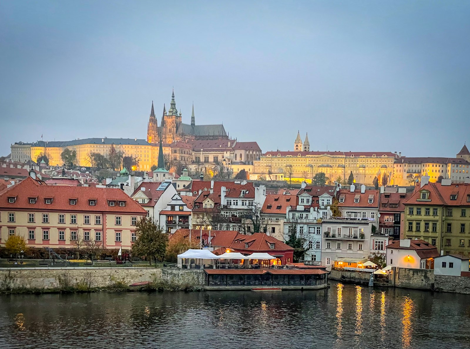 Prague's red rooftops, church spires and castle rising above the Vltava river at golden hour